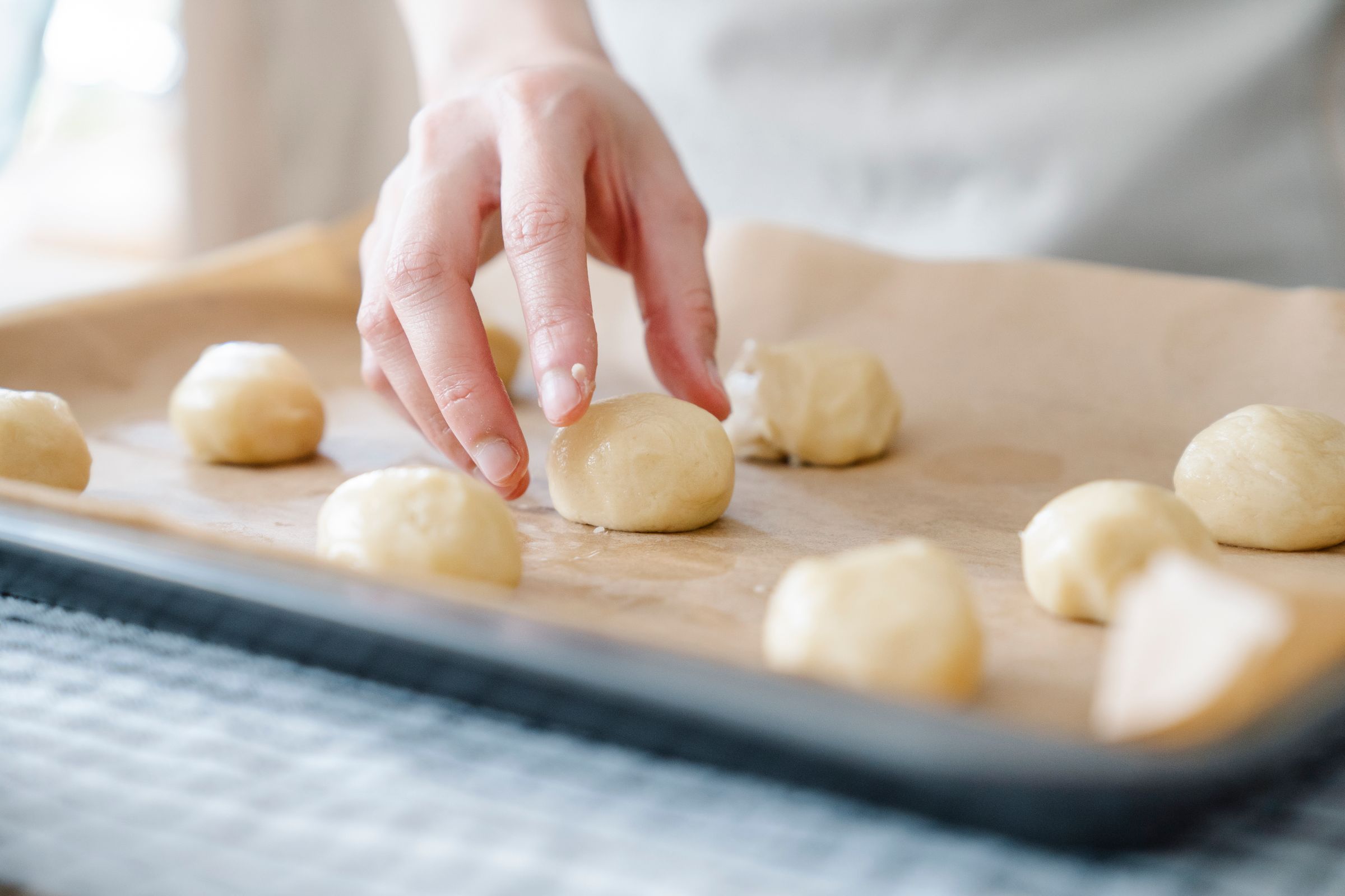 En hand lägger degbullar på en plåt med bakplåtspapper.